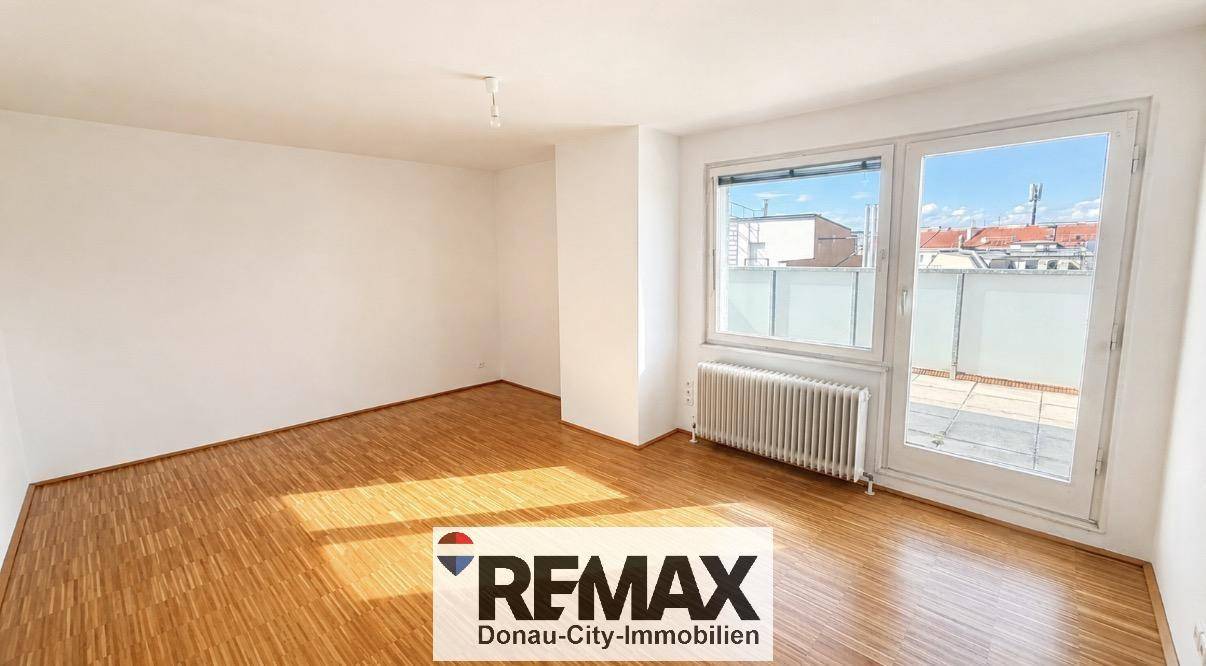 Helles, leeres Zimmer mit Holzparkettboden und Zugang zu einer Außenterrasse.