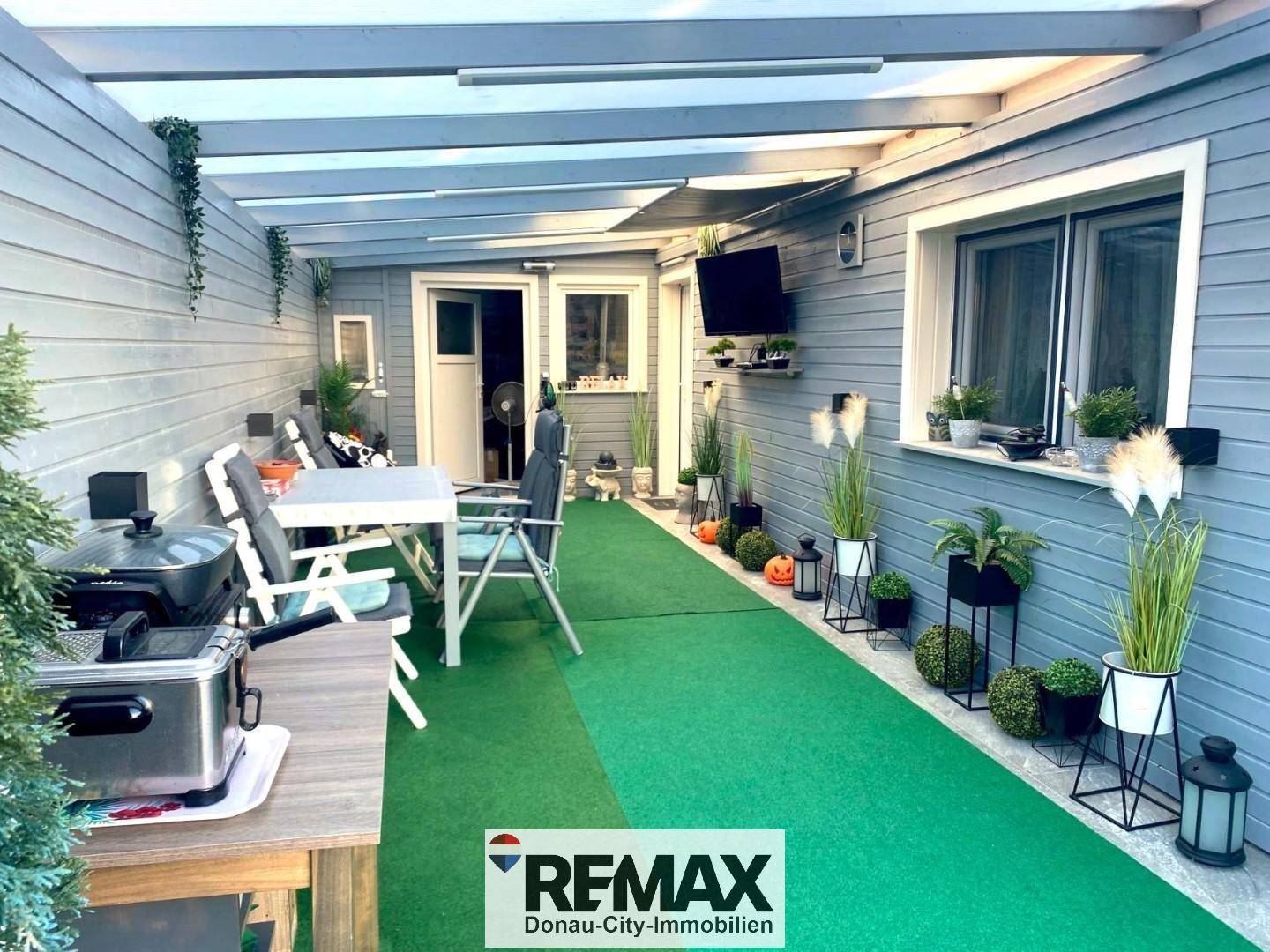 Überdachte Terrasse mit Kunstrasen, Essbereich und Dekoration, ideal für entspannte Stunden im Freien.