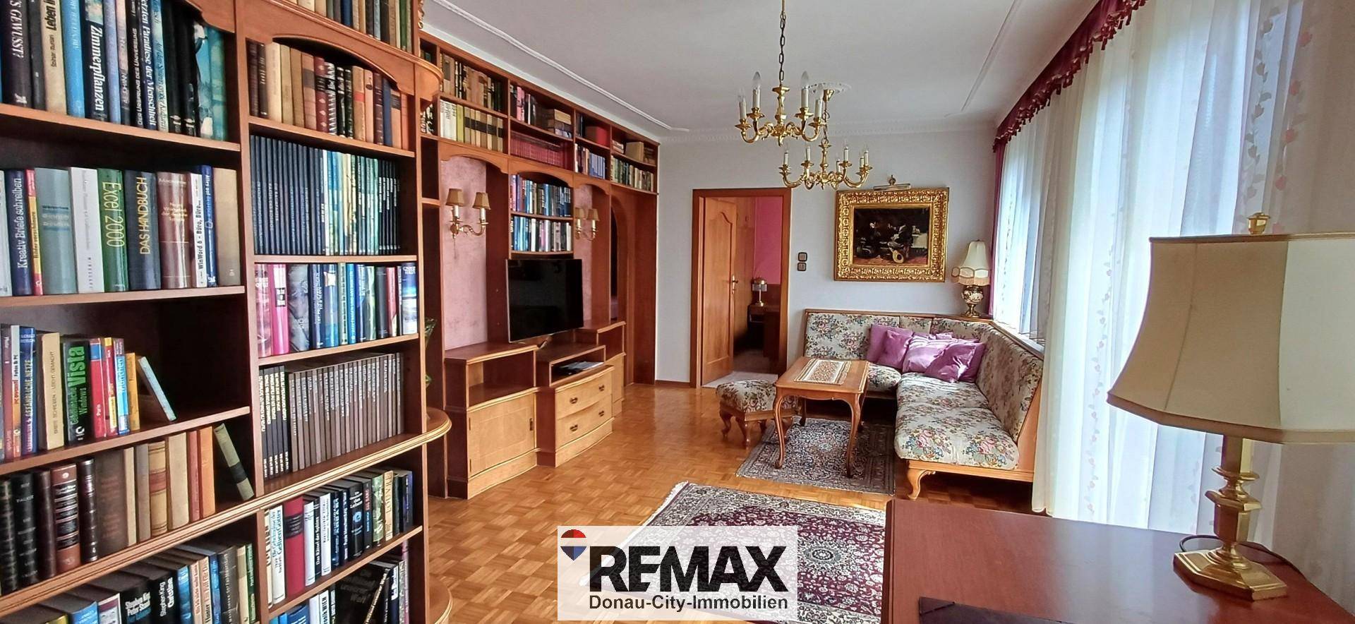 Elegantes Wohnzimmer mit großen Bücherregalen, bequemen Sofas und klassischem Kronleuchter.
