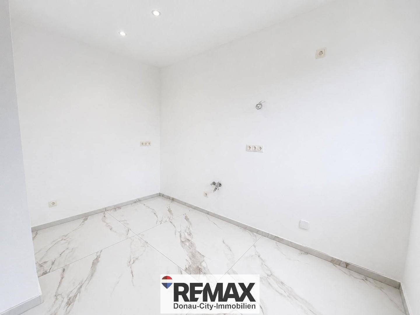 Leerer Raum mit eleganten Marmorfliesen und Anschlüssen für eine mögliche Kücheninstallation.