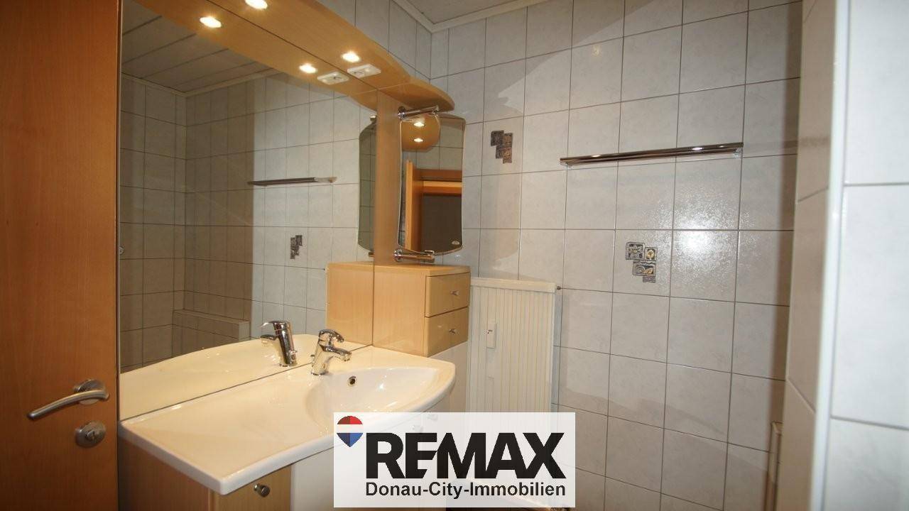 Badezimmer mit modernem Waschbecken und großem Spiegel, hell gefliest.