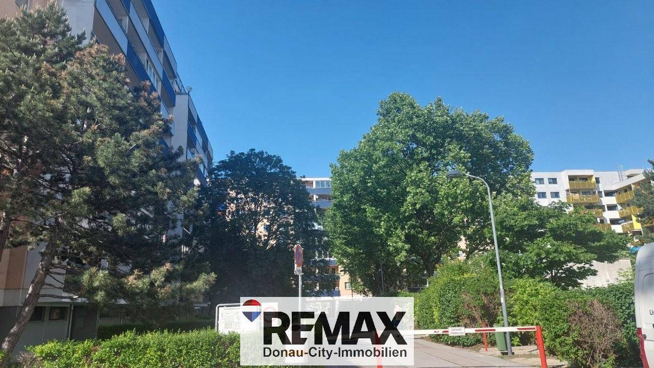 Wohngebäude umgeben von Bäumen und Grünflächen unter strahlend blauem Himmel.