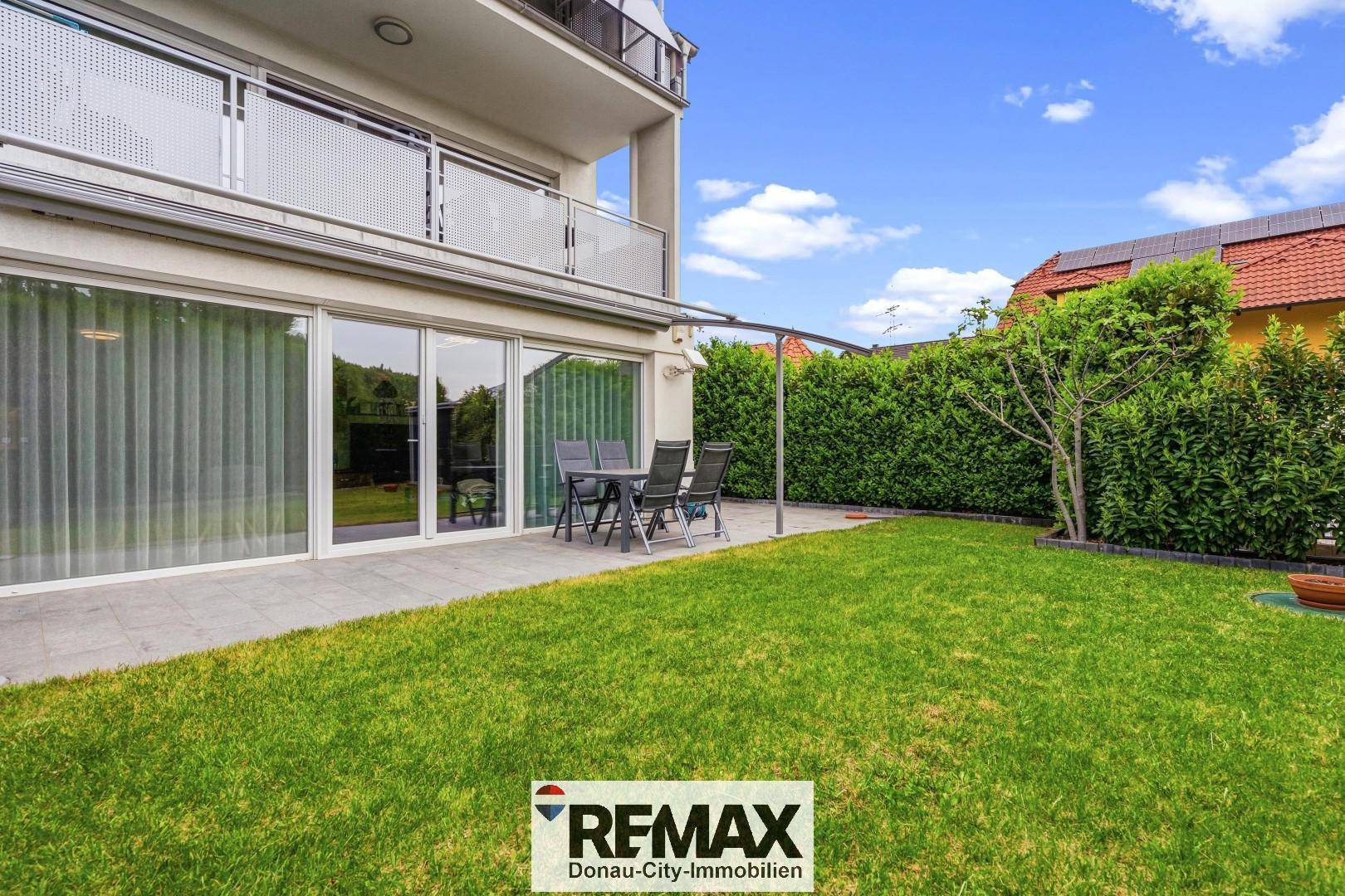 Sonniger Gartenbereich mit Terrasse, Rasenfläche und Hecke, ideal für Entspannung im Freien.