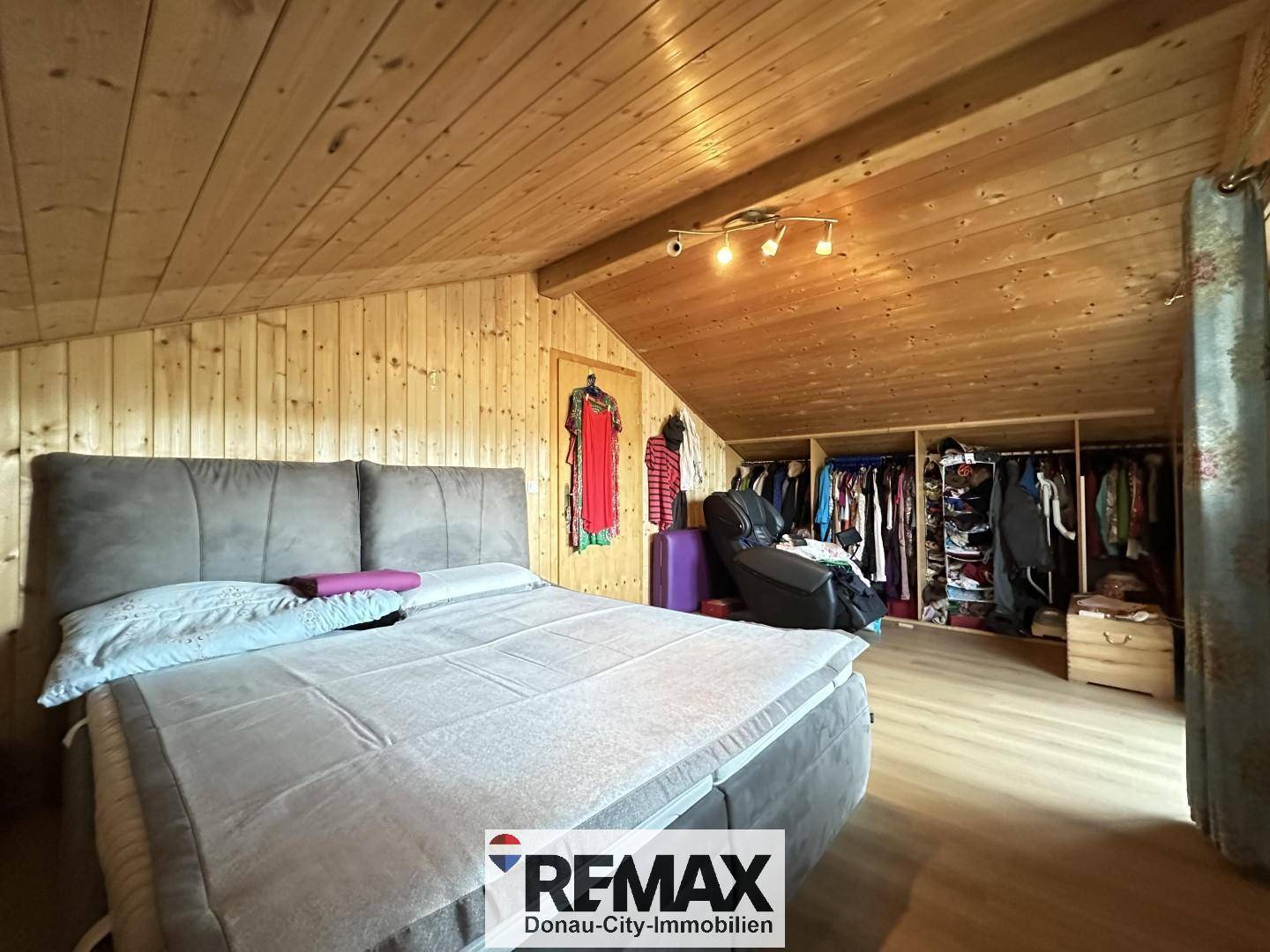 Schlafzimmer im Dachgeschoss mit Holztäfelung, Dachschräge und offenem Kleiderschrank.
