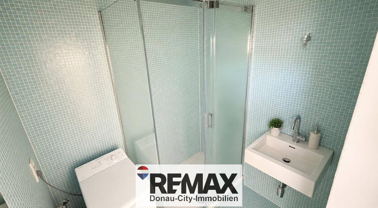 Modernes Badezimmer mit hellblauen Mosaikfliesen, Dusche und Waschbecken.