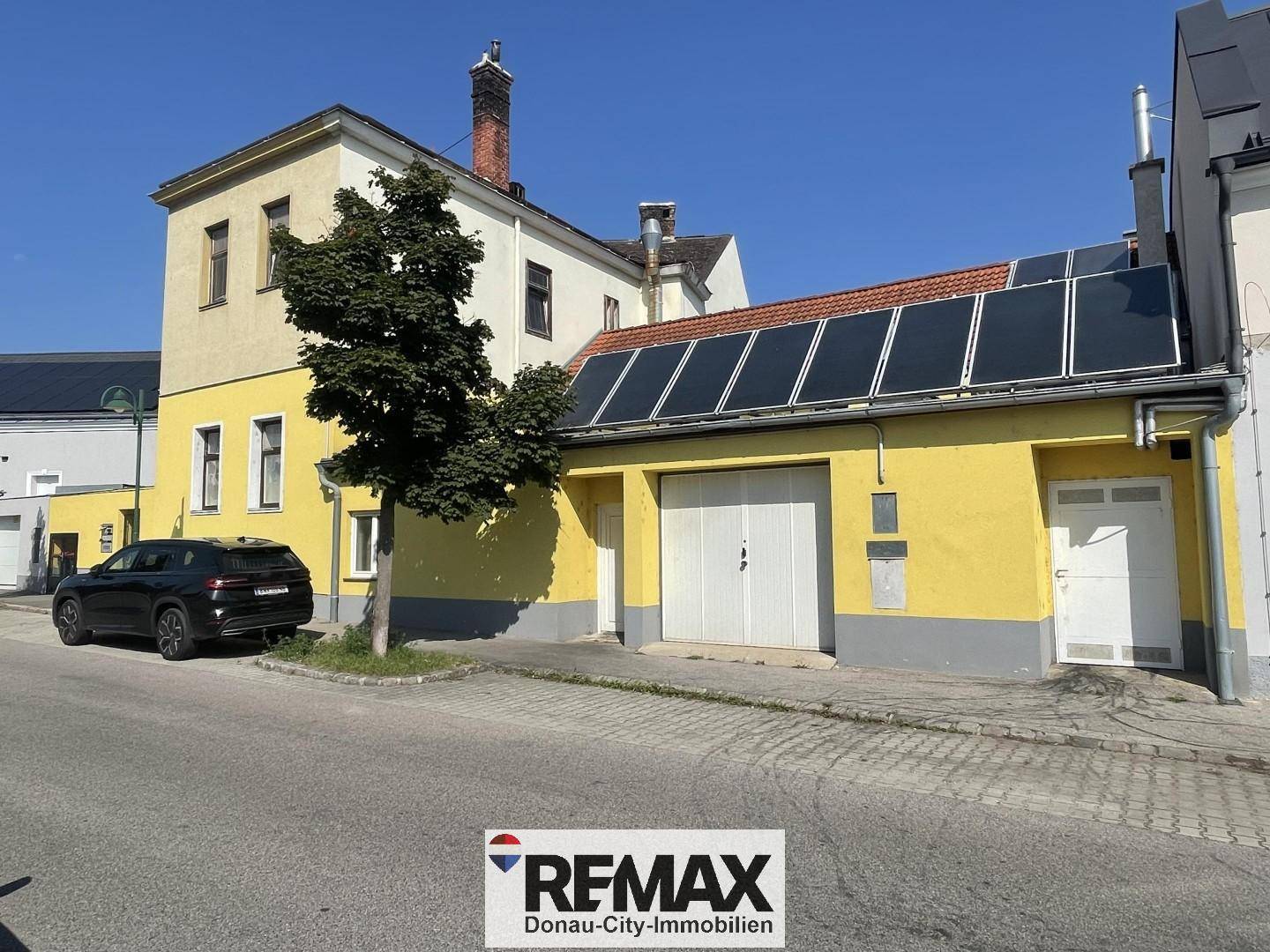 Seitenansicht des Gebäudes mit gelber Fassade, Garagentoren und Solarpaneelen auf dem Dach.