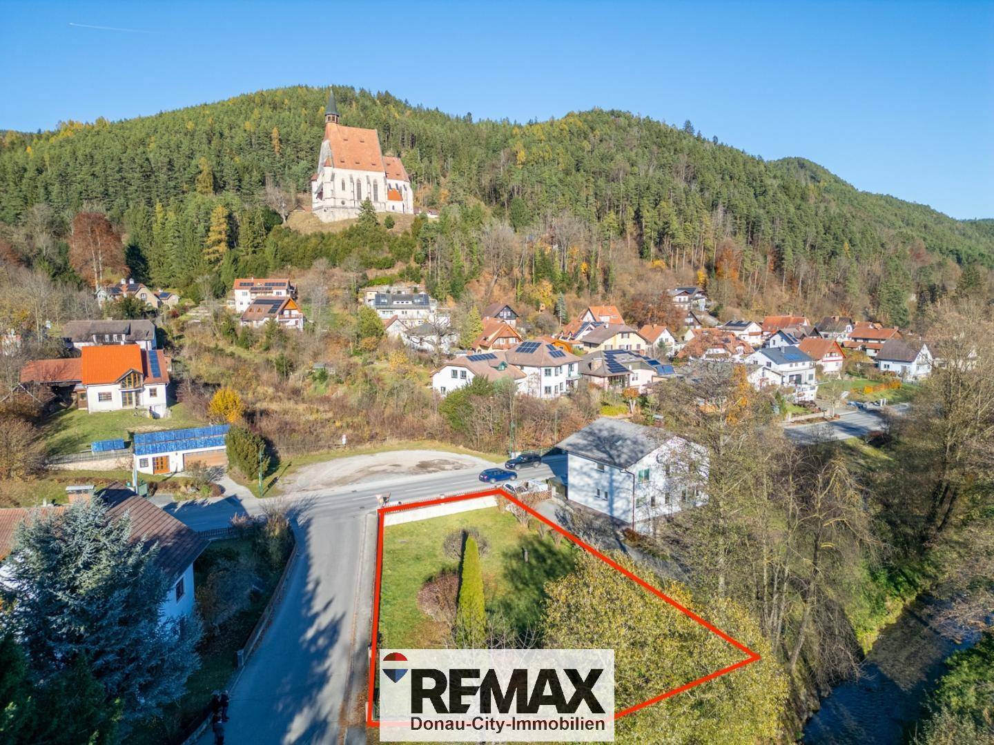 Luftaufnahme eines Grundstücks mit roter Umrandung, umgeben von Häusern und einer Kirche auf einem Hügel.