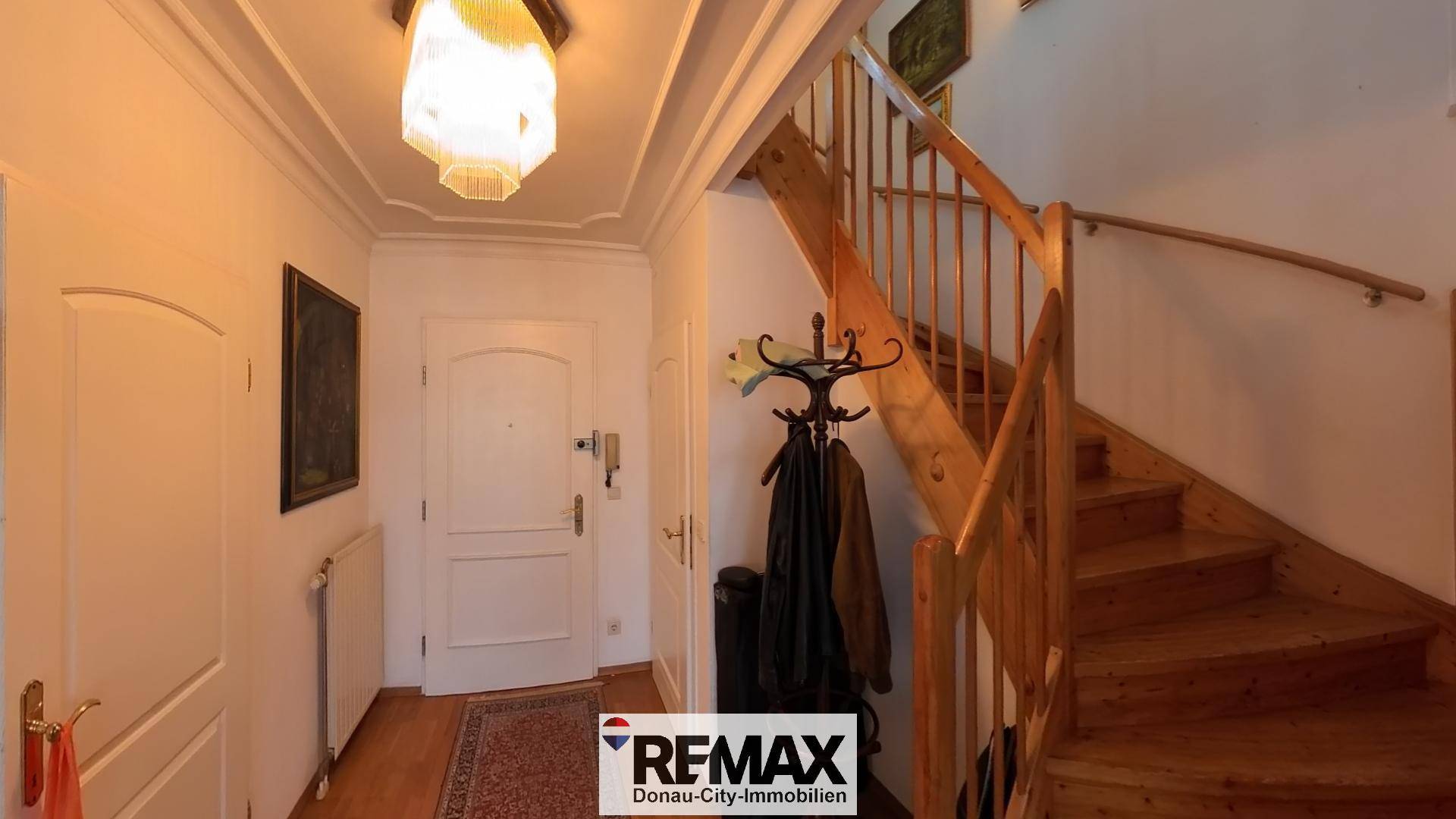 Eingangsbereich mit Holztreppe, Garderobe und heller Deckenbeleuchtung.