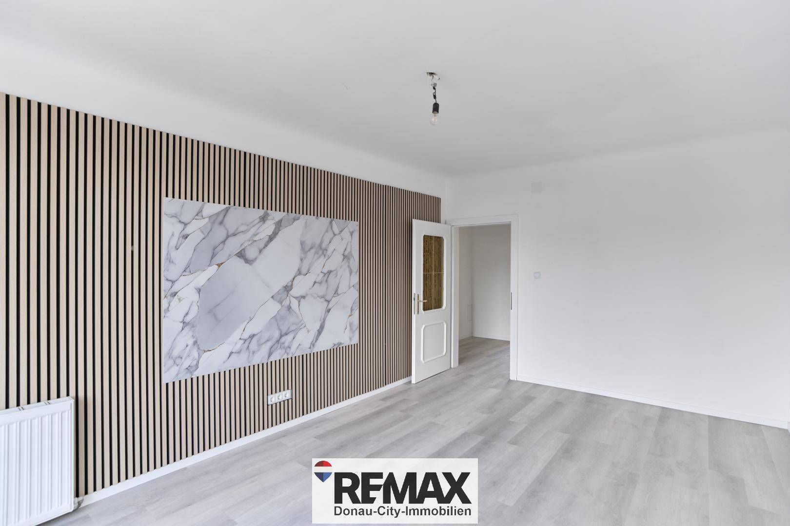 Geräumiger Wohnbereich mit hellem Laminatboden und dekorativer Wandgestaltung, ideal für individuelle Einrichtung.