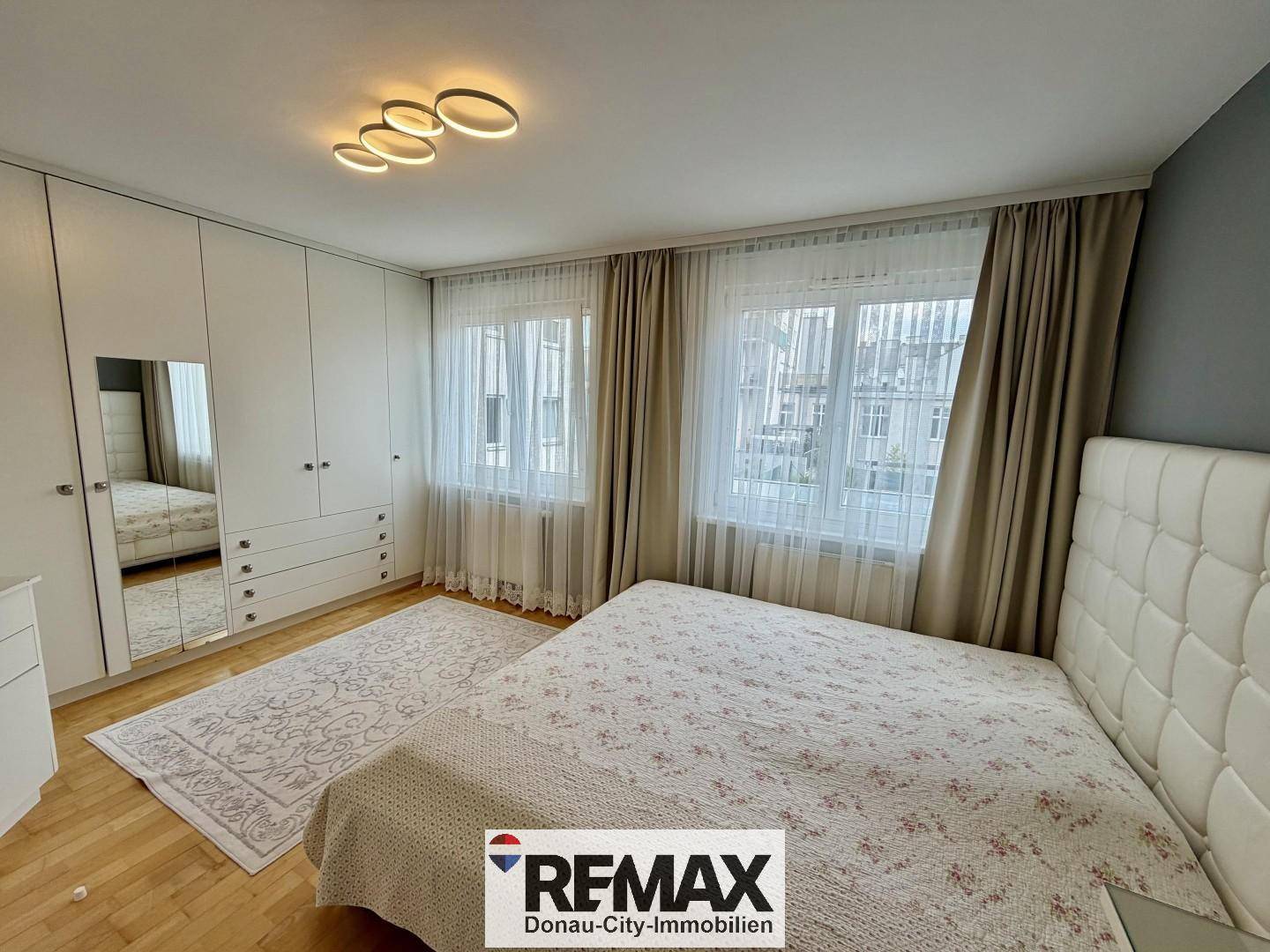 Schlafzimmer mit großem Doppelbett, Einbauschränken und viel Tageslicht durch die Fenster.