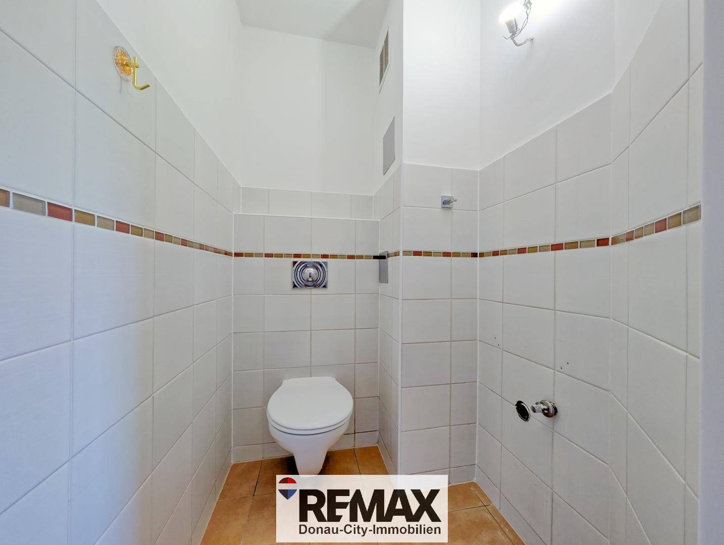 Gefliestes Gäste-WC mit wandhängender Toilette und farbigen Dekorstreifen an den Wänden.