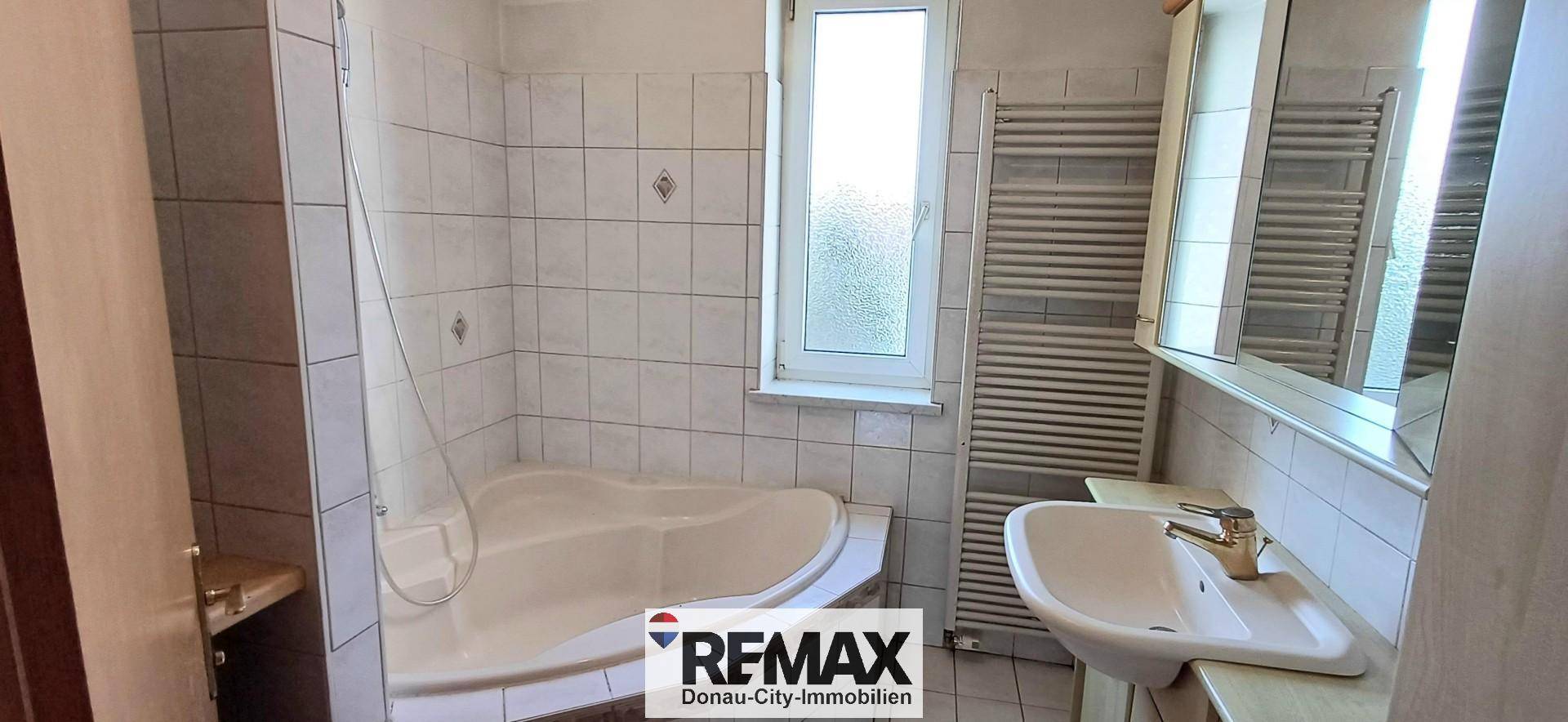 Gefliestes Badezimmer mit Badewanne, Waschbecken und einem Fenster für natürliche Belüftung.