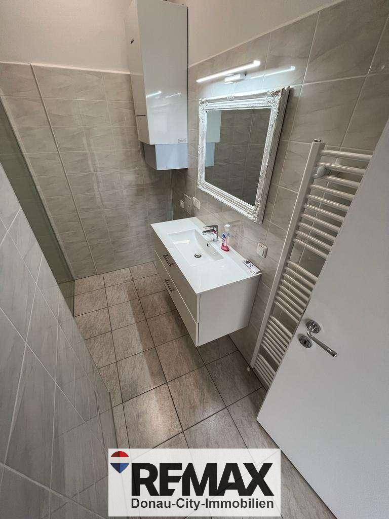 Modernes Badezimmer mit Fliesenboden, Waschtisch und beheiztem Handtuchhalter.