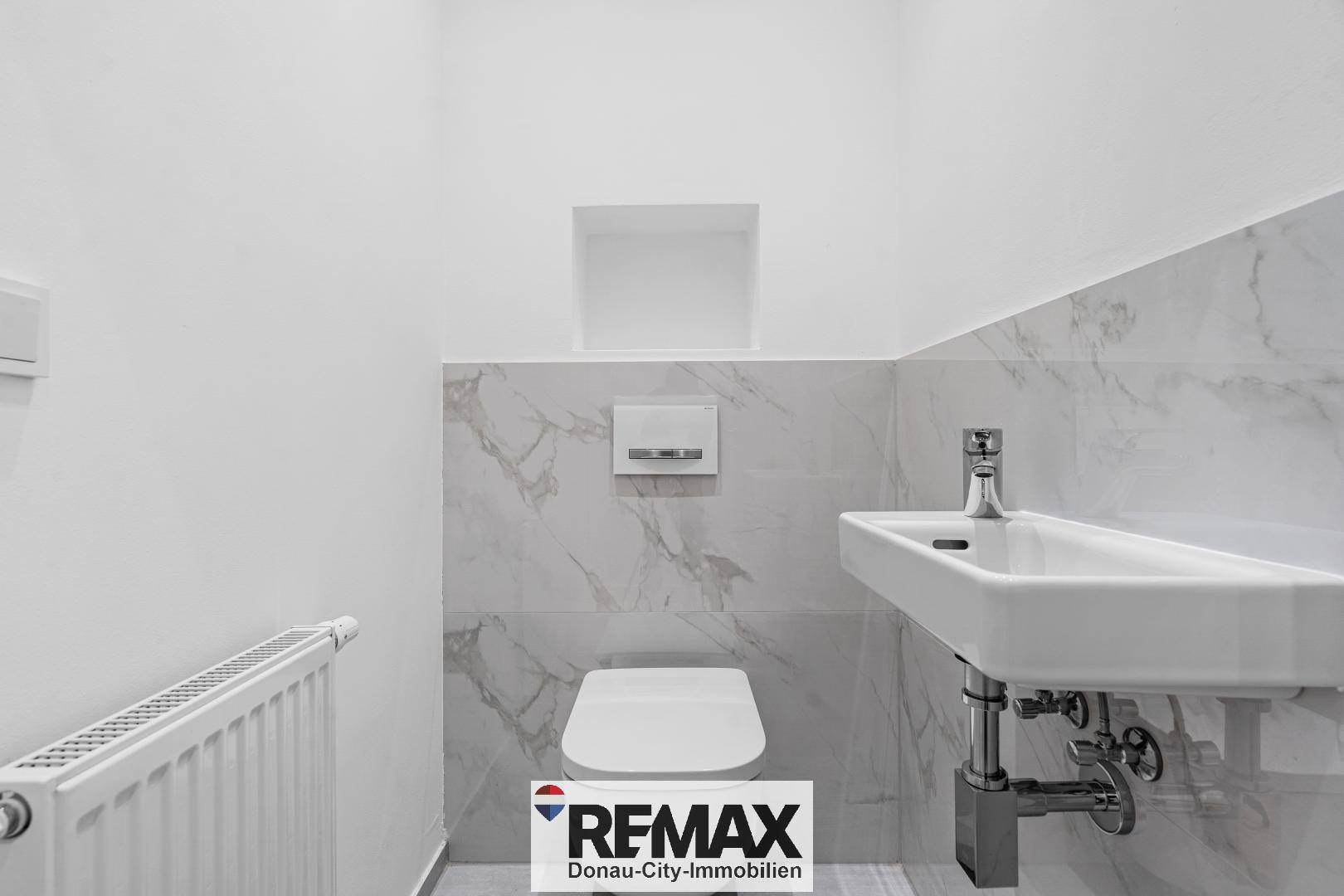 Modernes Gäste-WC mit Wand-WC, Einzelwaschbecken und Fliesen in Marmoroptik.