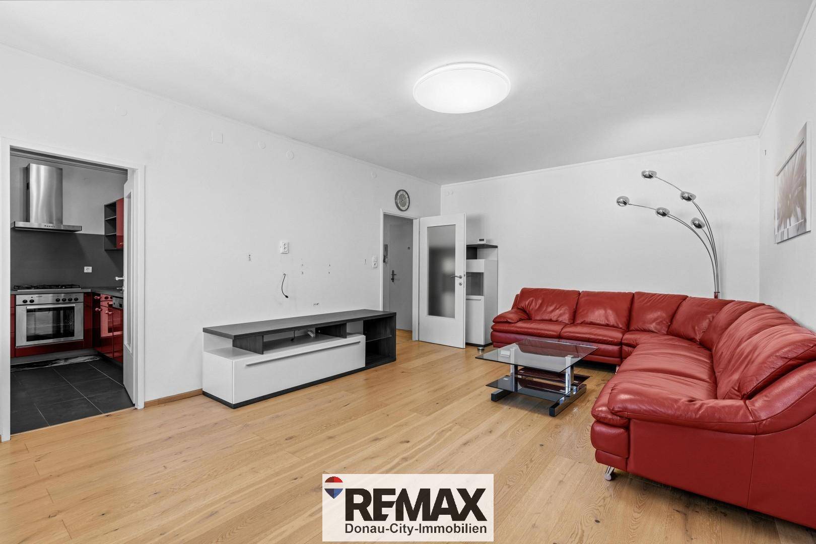 Geräumiges Wohnzimmer mit rotem Ledersofa, Couchtisch und hellem Laminatboden, bereit zur individuellen Gestaltung.