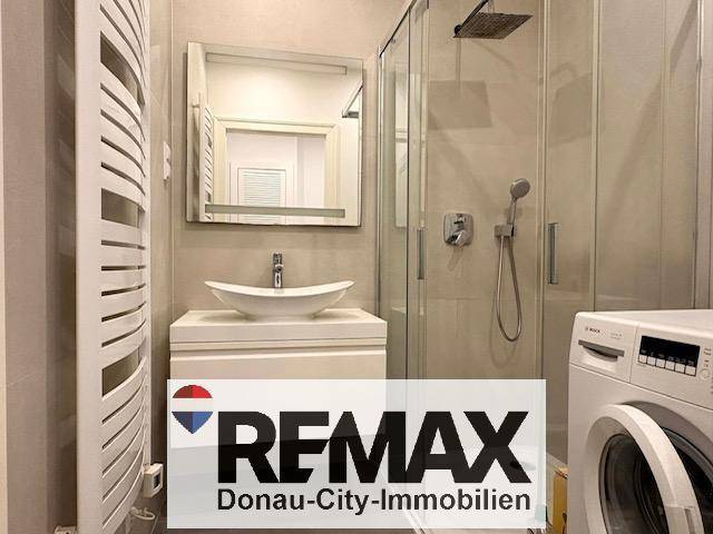 Modernes Badezimmer mit ebenerdiger Dusche, Regendusche, Waschbecken und praktischem Handtuchheizkörper.