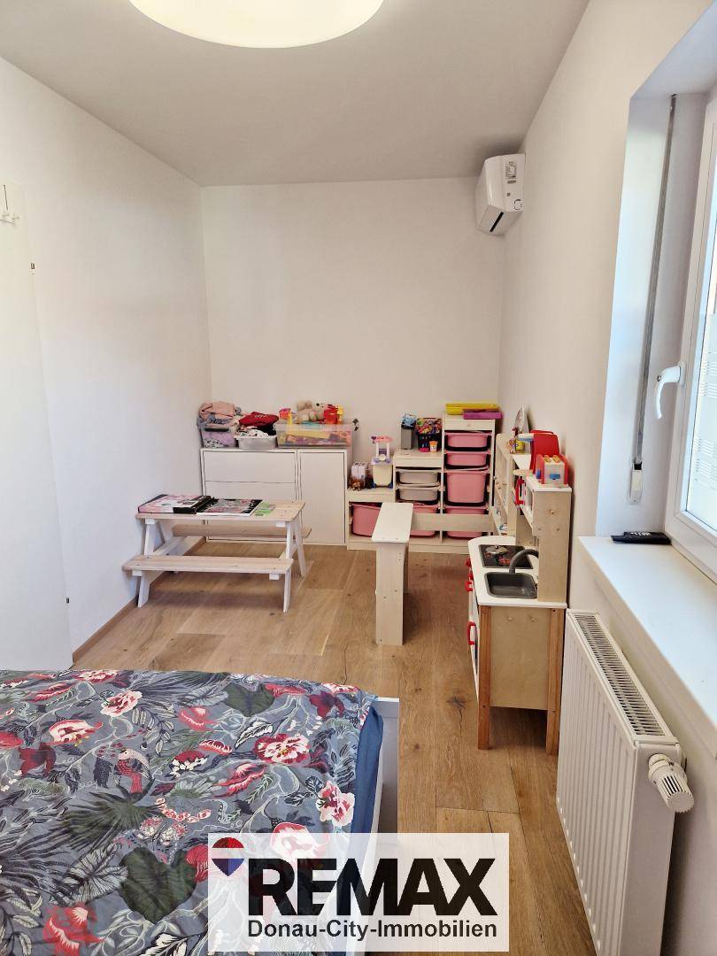 Kinderzimmer mit Bett, Spielküche, Holzfußboden und Klimaanlage, hell und freundlich gestaltet.