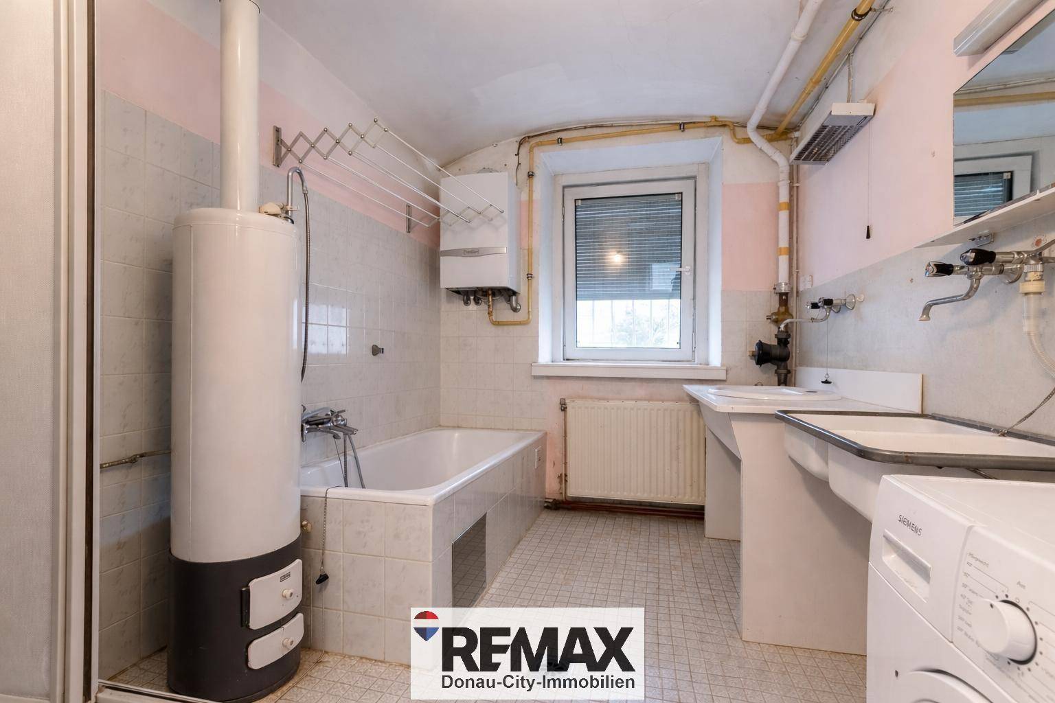 Älteres Badezimmer mit Badewanne, Waschbecken und Boiler, renovierungsbedürftig.
