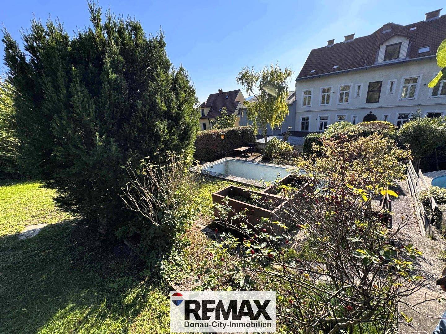 Großer Gartenbereich mit viel Grün, Sträuchern und einem alten Wasserbecken, bietet Entwicklungspotenzial.