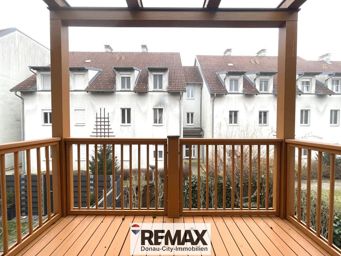 Holzbalkon mit Blick auf die umliegenden Gebäude und grüne Bepflanzung.