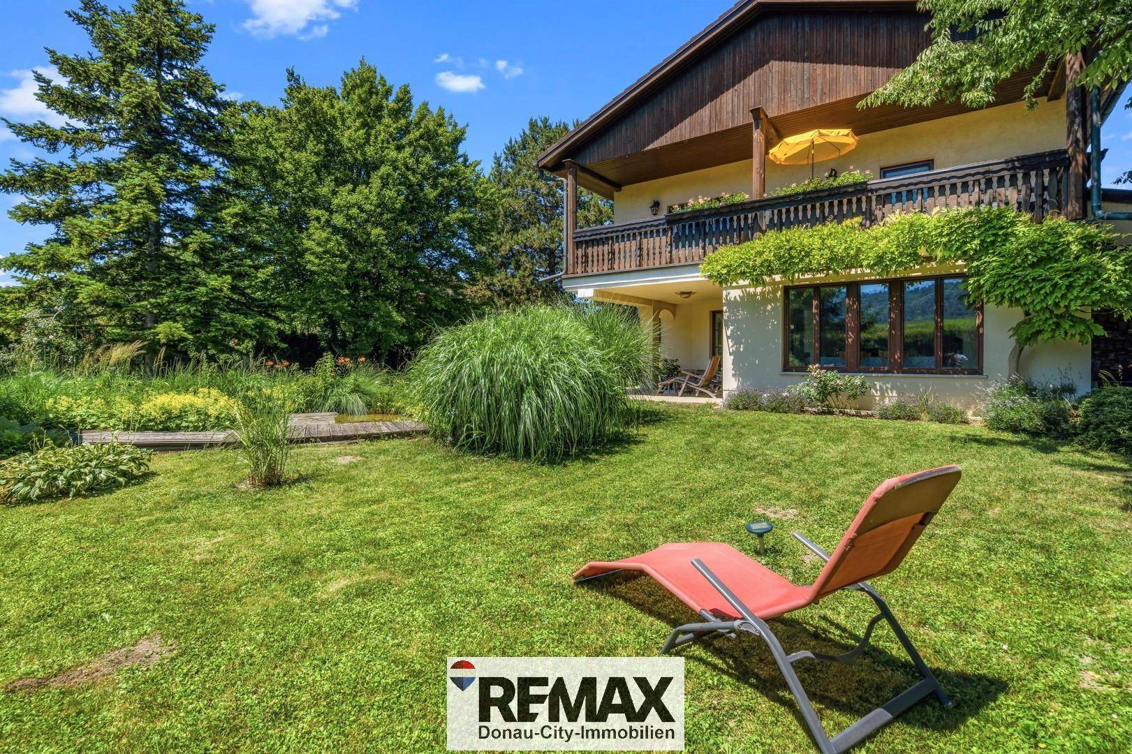 Großer, gepflegter Garten mit Rasenfläche, Liegestuhl und Blick auf das Haus.