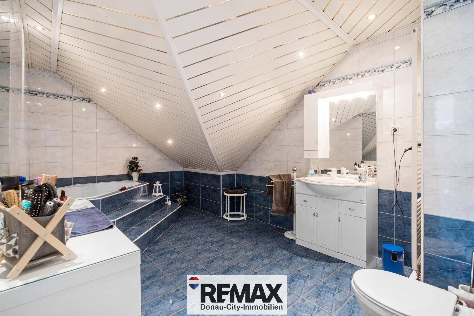 Geräumiges Badezimmer im Dachgeschoss mit Badewanne, Waschtisch und blauen Fliesen unter der Dachschräge.