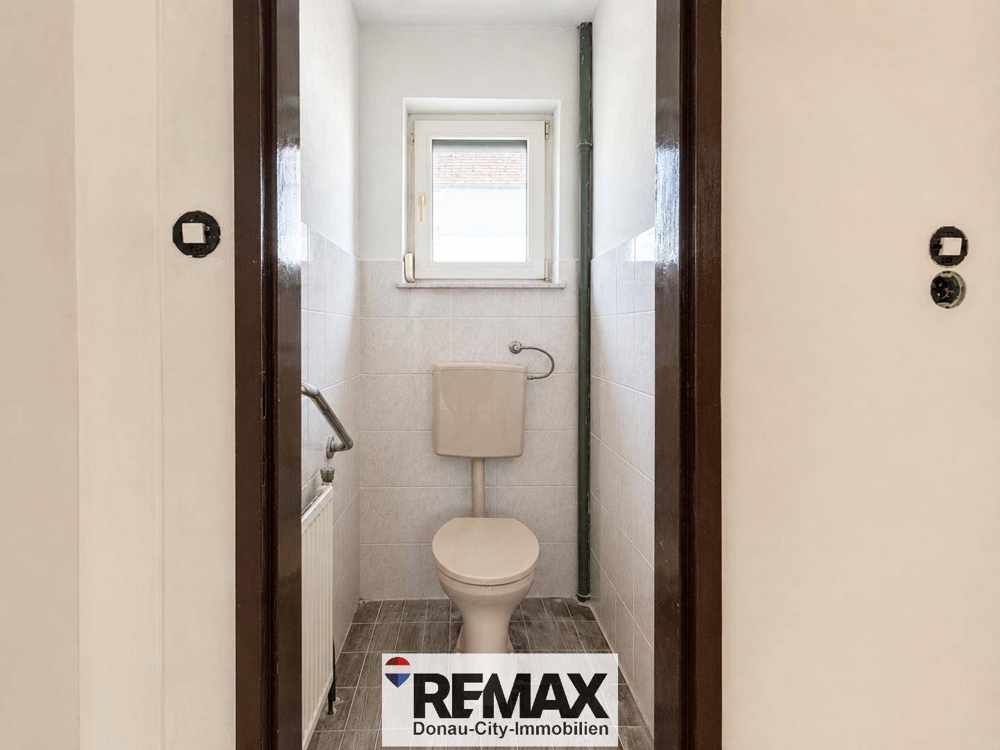 Separate Toilette mit Fenster, Wand-WC und Fliesenboden.