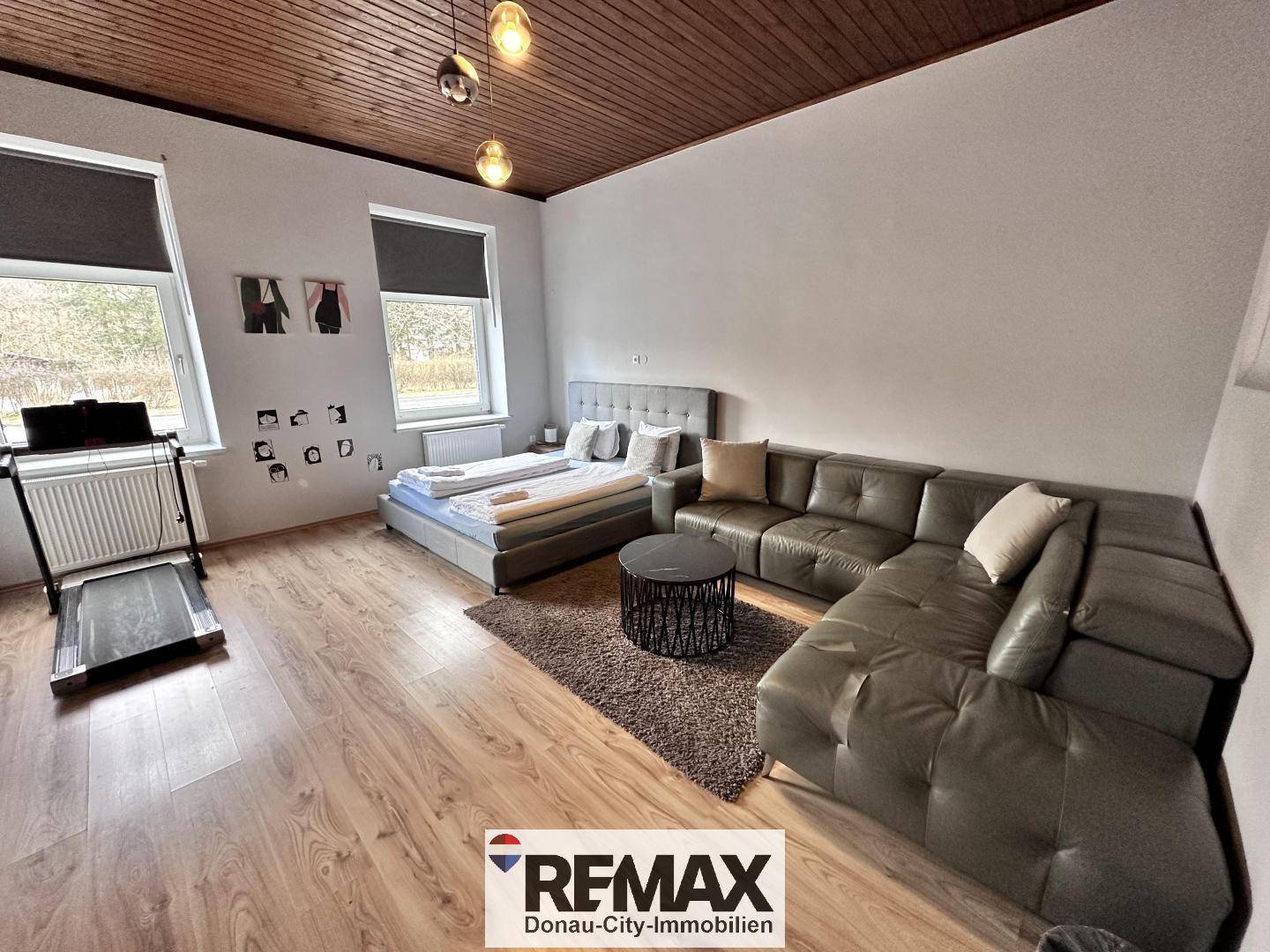 Geräumiger Wohnbereich mit Holzboden, großem Sofa, Bett und Fitnessgerät.