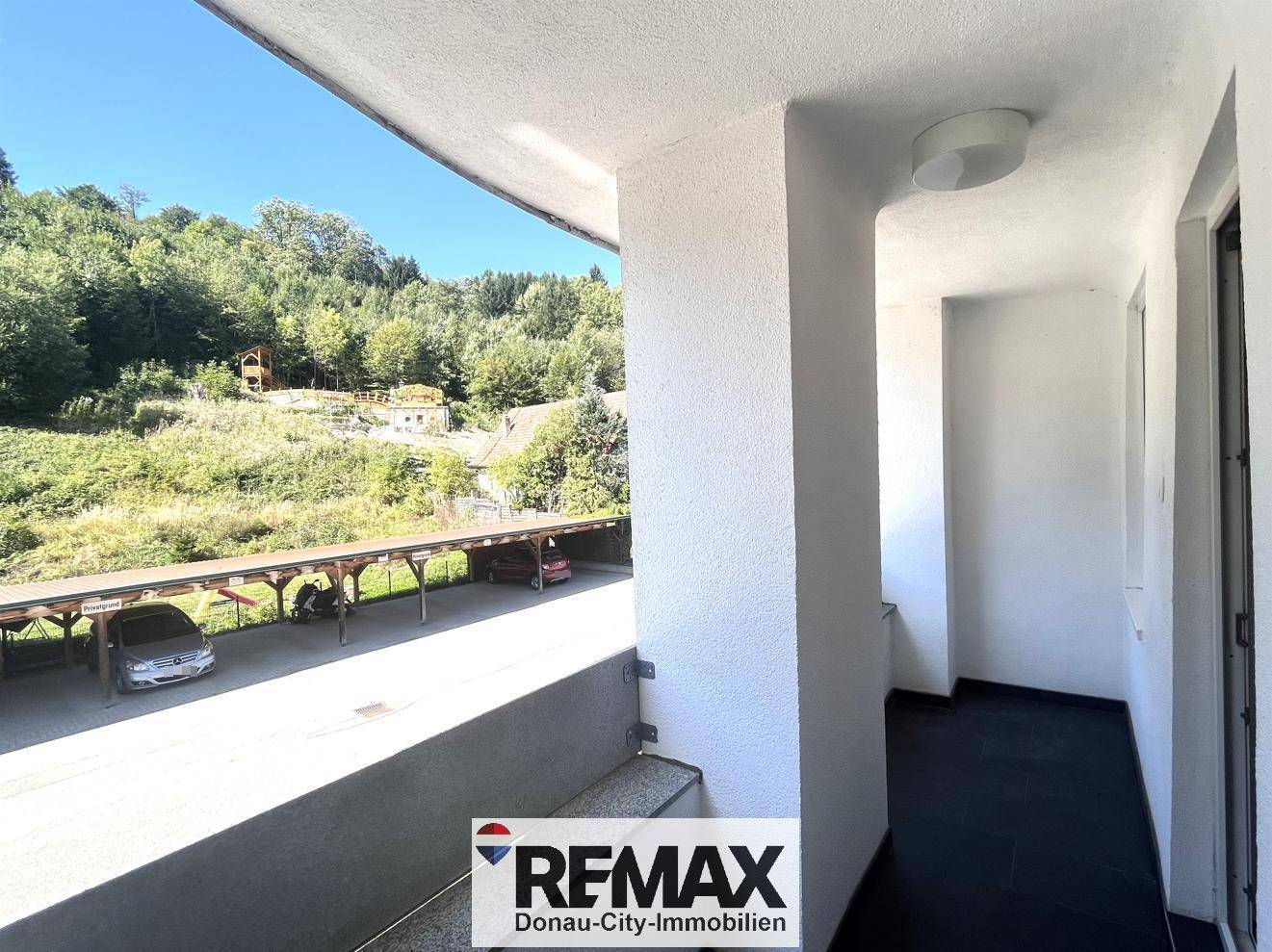 Überdachte Loggia mit Blick auf einen Carport und die bewaldete Umgebung.