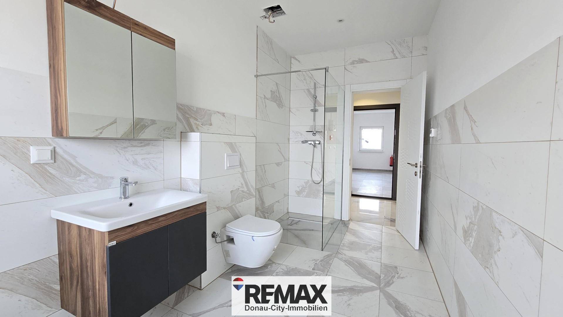 Modernes Badezimmer mit begehbarer Dusche, eleganten Fliesen und Waschtisch mit Unterschrank.