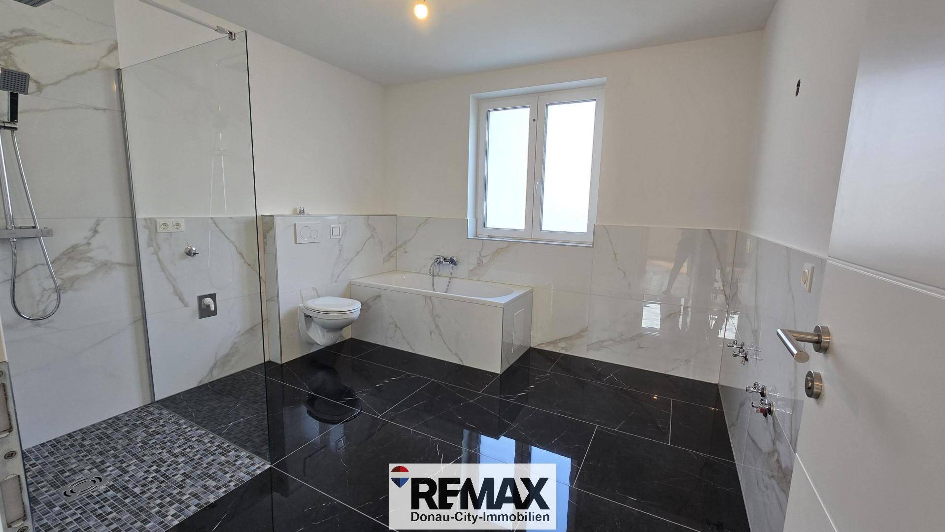 Modernes Badezimmer mit schwarzen Fliesen, weißer Badewanne und großer begehbarer Dusche.