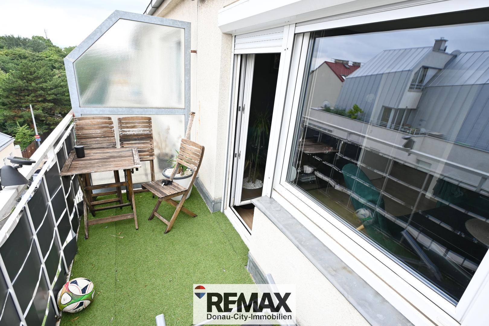 Kleiner Balkon mit Kunstrasen, Holztisch und Stühlen, ideal für entspannte Stunden im Freien.
