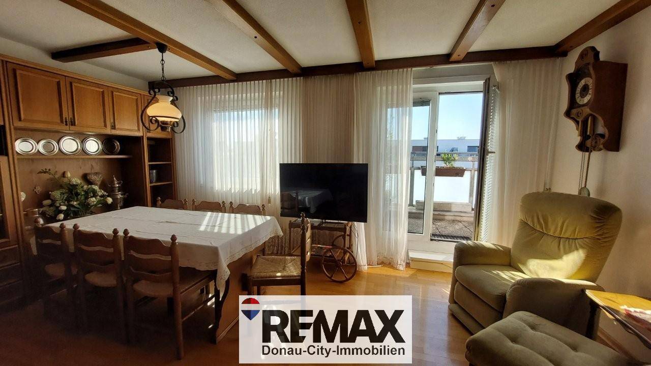 Gemütlicher Wohn-Essbereich mit Holzbalken, Zugang zum Balkon und bequemen Sesseln.