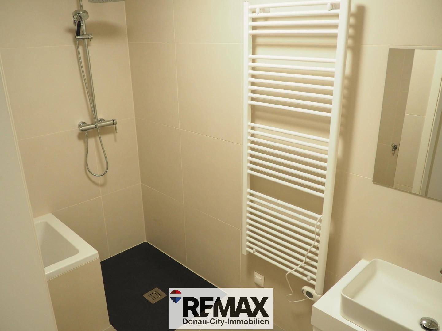 Helles Badezimmer mit Dusche, beheiztem Handtuchhalter und modernem Waschbecken.
