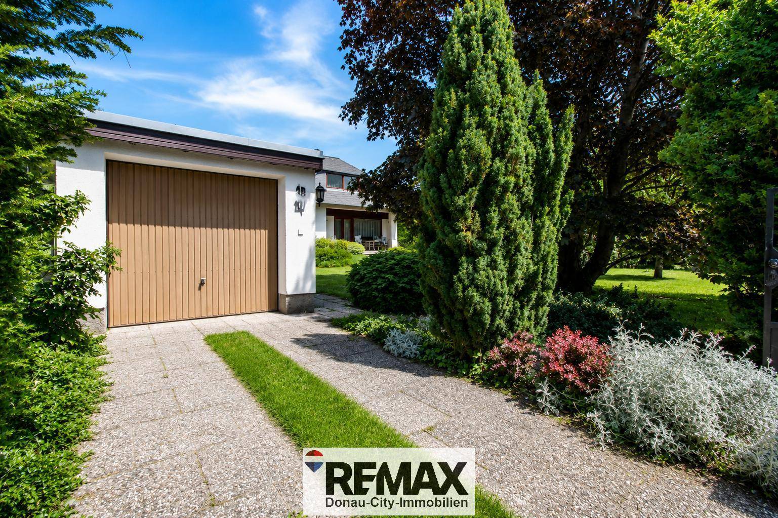 Einfahrt zum Haus mit Garage, gepflastertem Weg und grüner Bepflanzung, bietet ausreichend Parkmöglichkeiten.