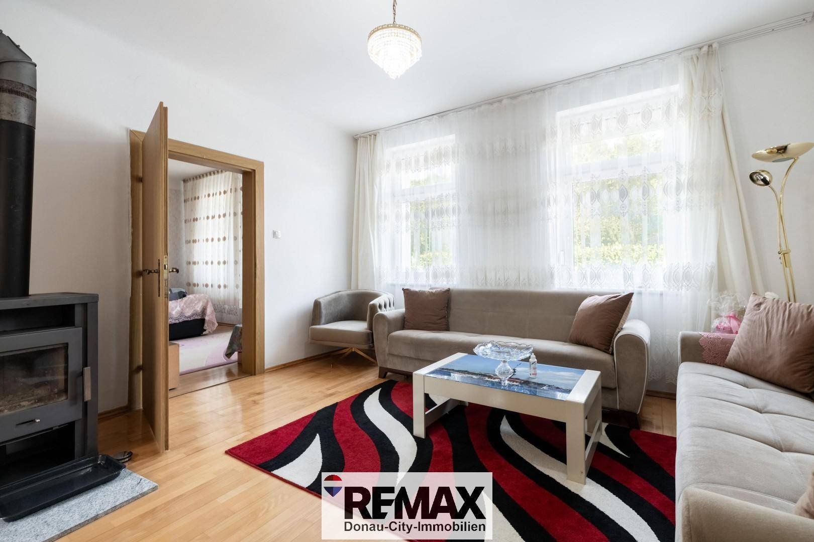 Gemütliches Wohnzimmer mit Holzofen, Parkettboden und hellen Fenstern.