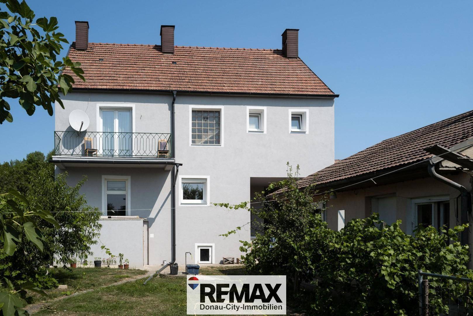 Rückansicht eines Wohnhauses mit Balkon und Gartenbereich unter blauem Himmel.