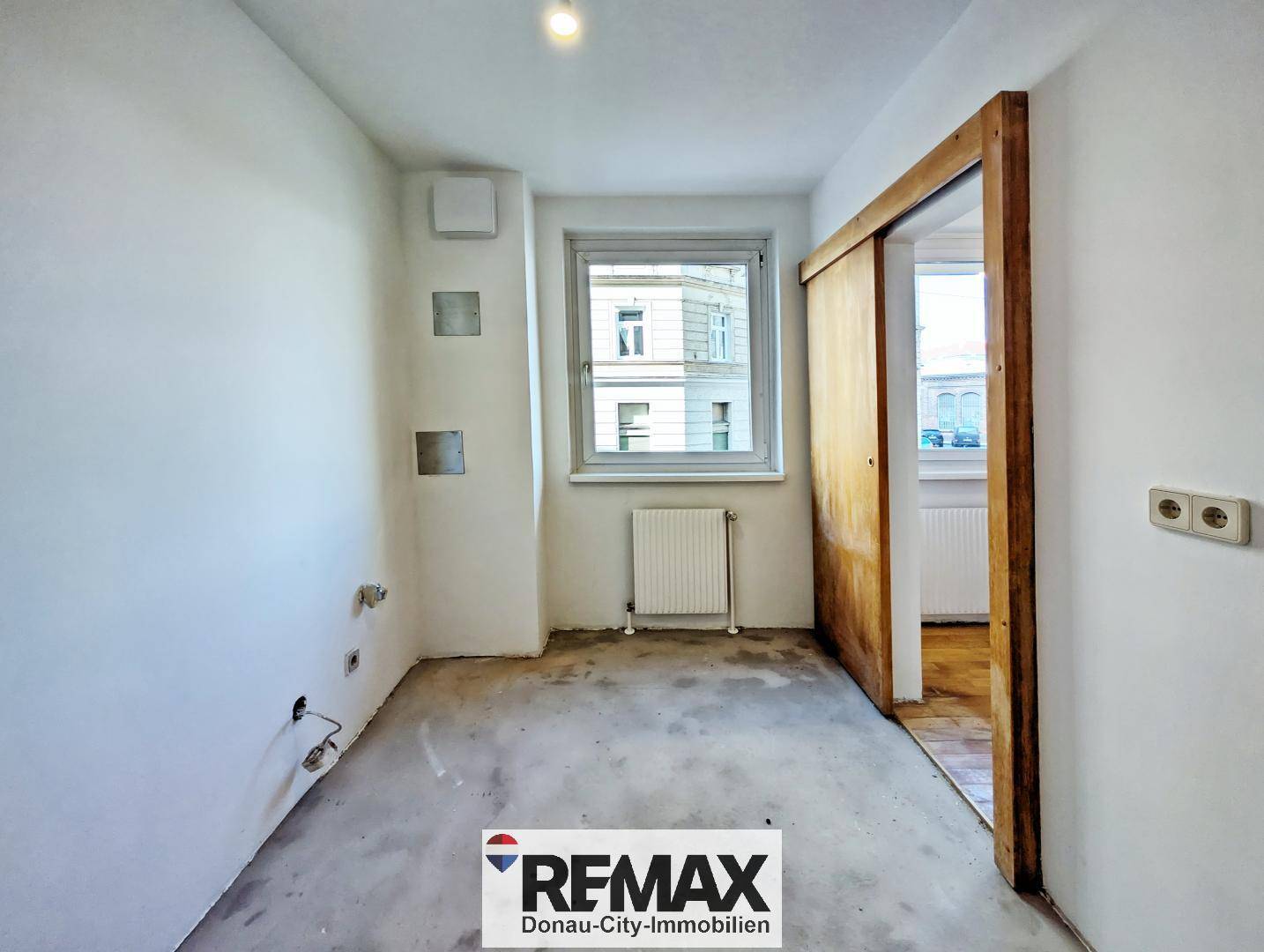 Leerer Küchenraum mit Rohanschlüssen und Fenster, bereit für die Installation einer neuen Einbauküche.