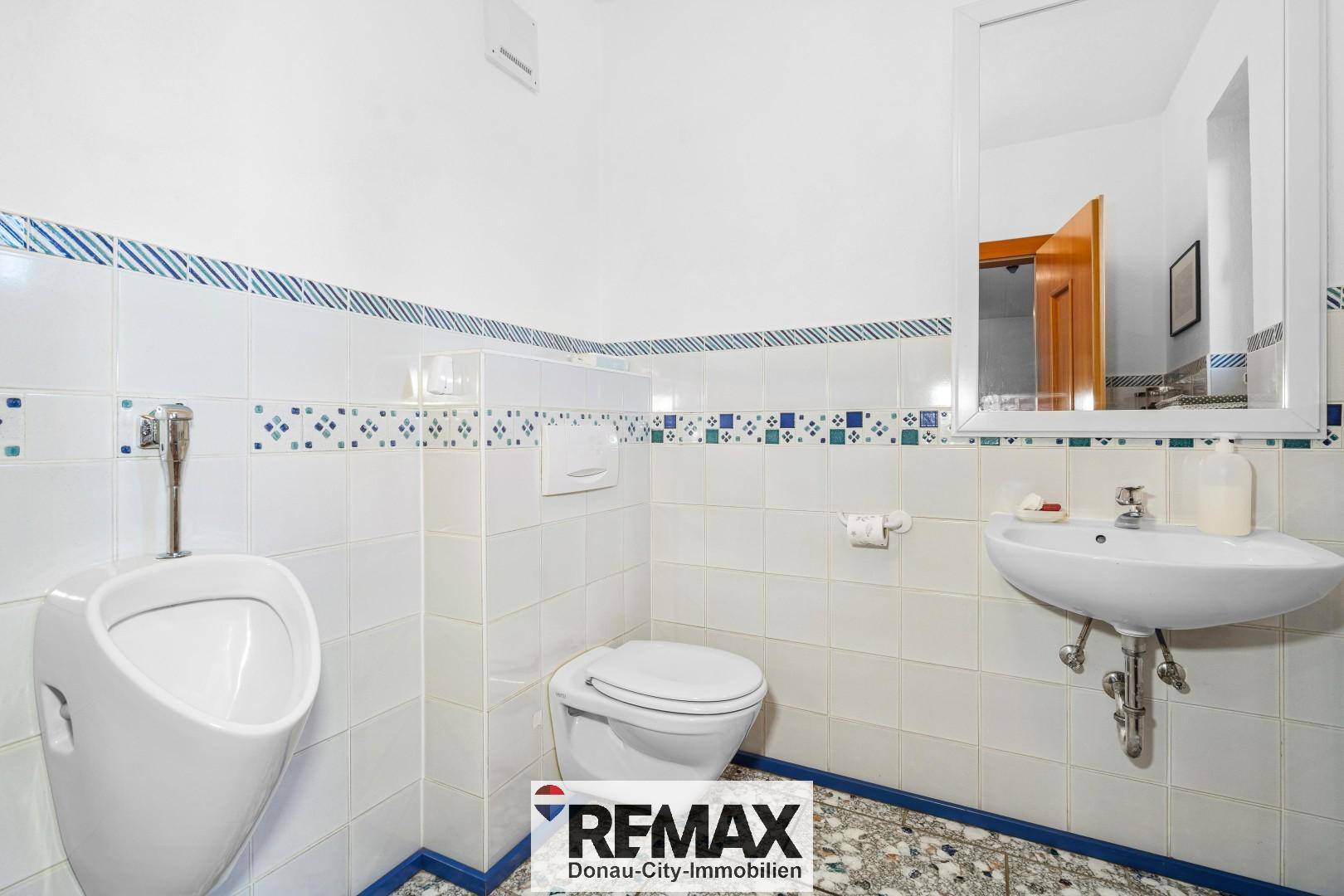 Kleines Gäste-WC mit Urinal, Waschbecken und Fliesenboden.