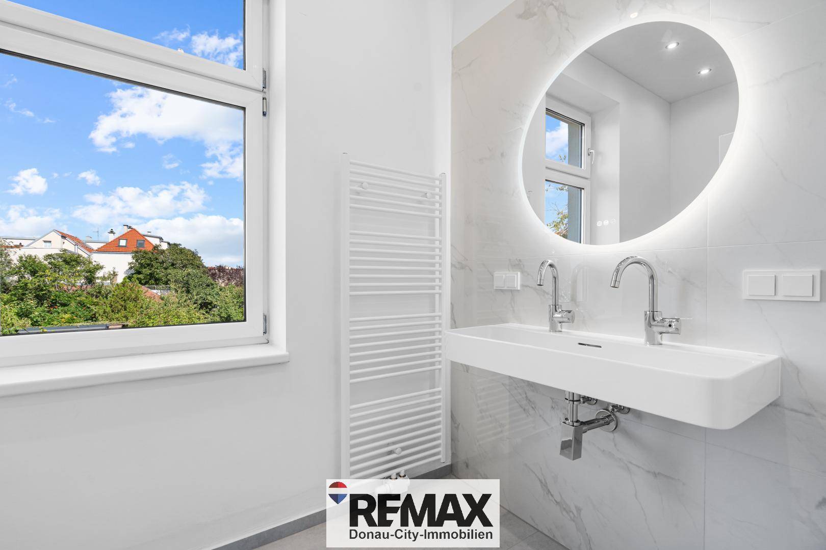 Modernes Badezimmer mit Doppelwaschbecken, beleuchtetem Spiegel und Fenster.