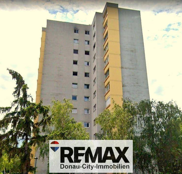 Hohes Mehrfamilienhaus mit gelben Akzenten und Bäumen im Vordergrund.