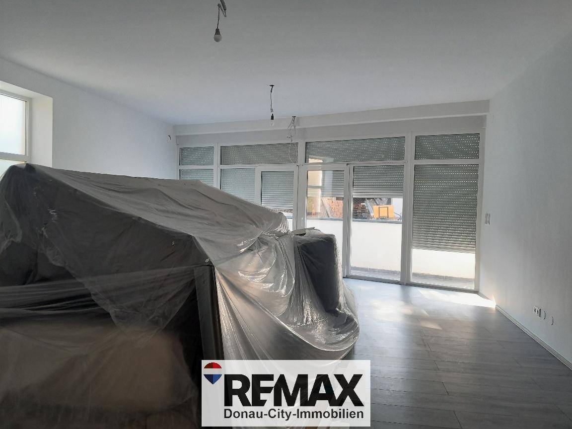 Geräumiges Wohnzimmer mit großen Fenstern und Rollläden, bereit für die Fertigstellung.