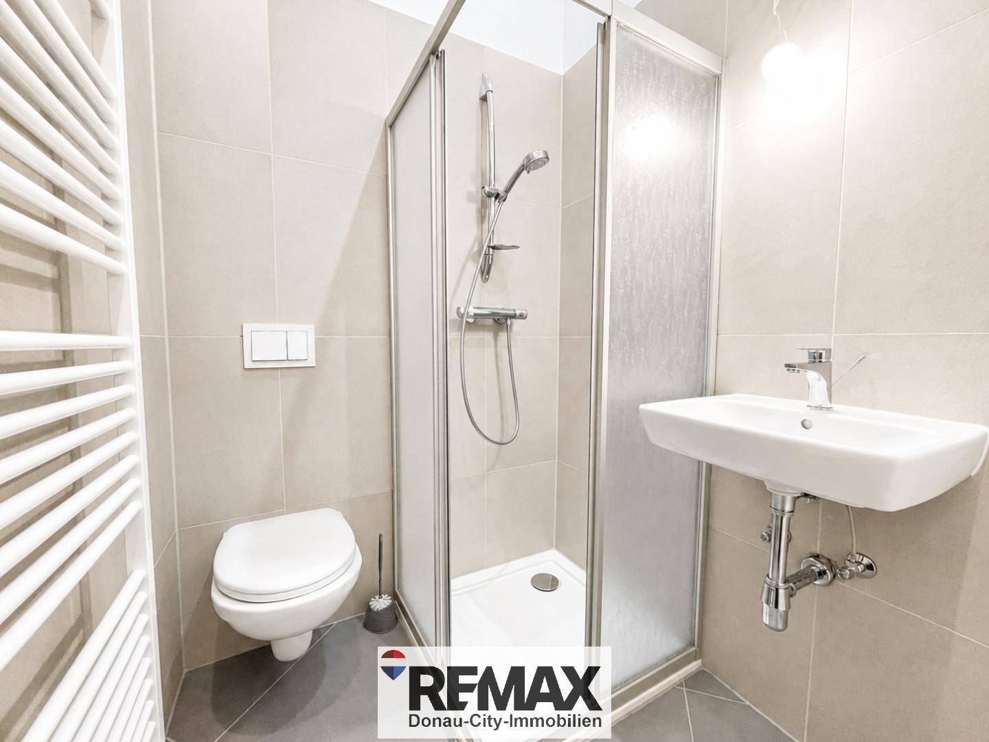 Modernes Badezimmer mit Duschkabine, WC, Waschbecken und beheiztem Handtuchhalter.