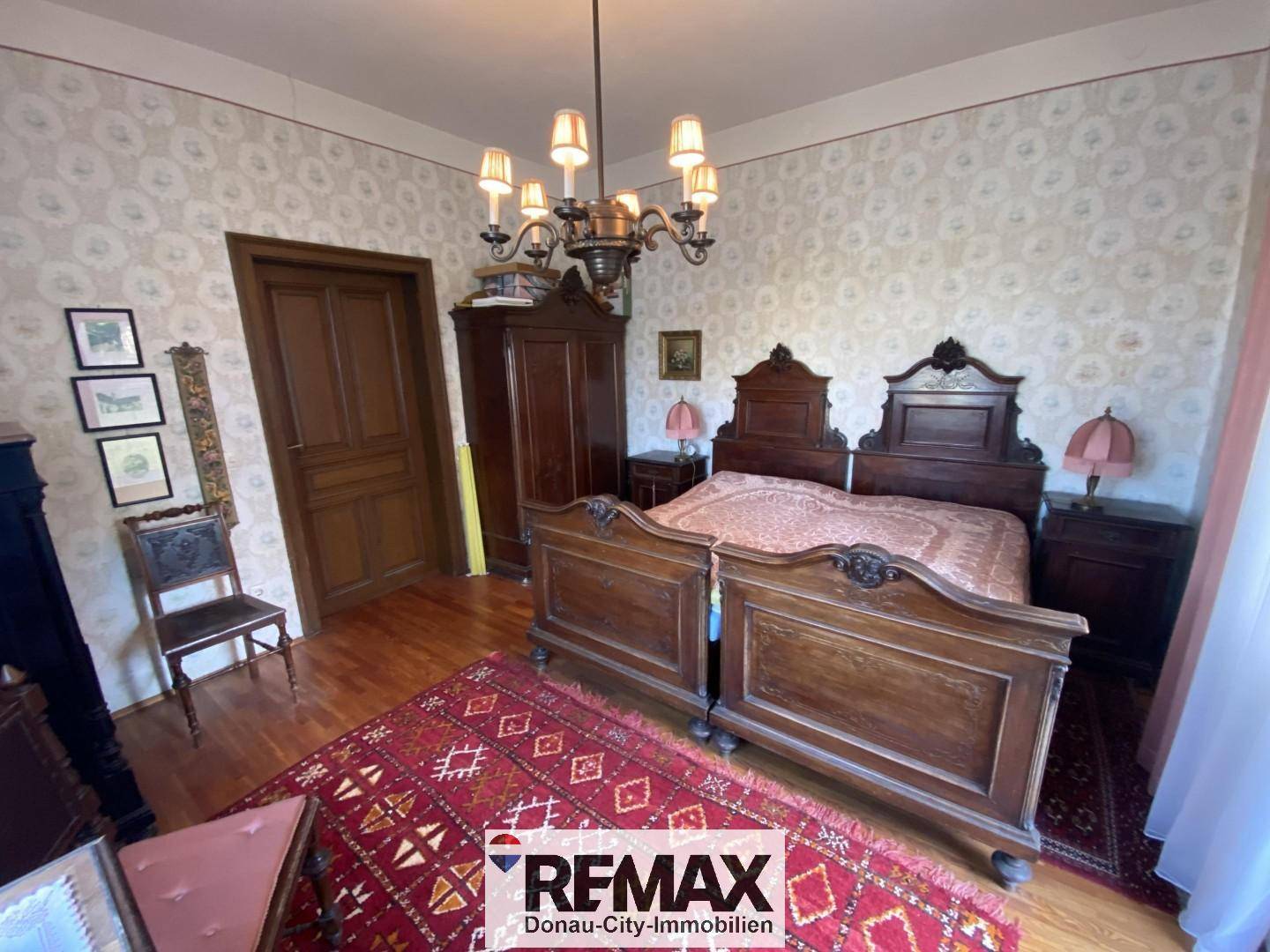 Geräumiges Schlafzimmer mit antiken Holzmöbeln, gemusterter Tapete und Kronleuchter.
