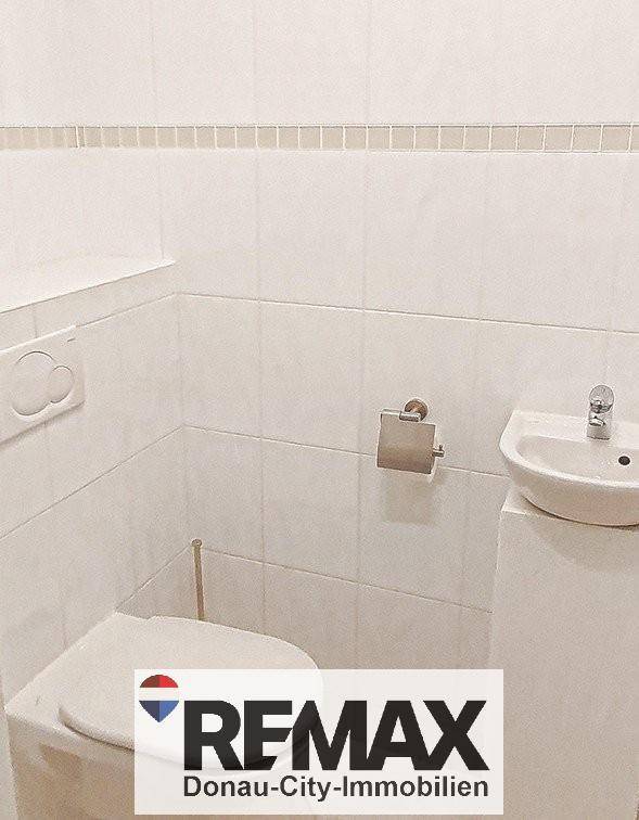 Separates WC mit Toilette und kleinem Handwaschbecken, gefliest in Weiß.