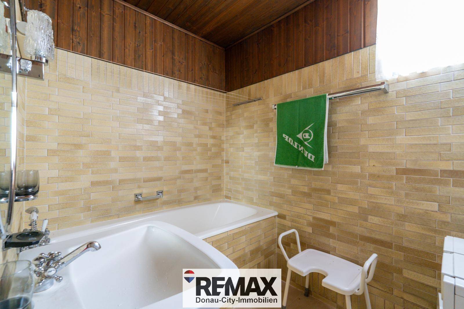 Badezimmer mit beigefarbenen Fliesen, Badewanne und Holzdecke.