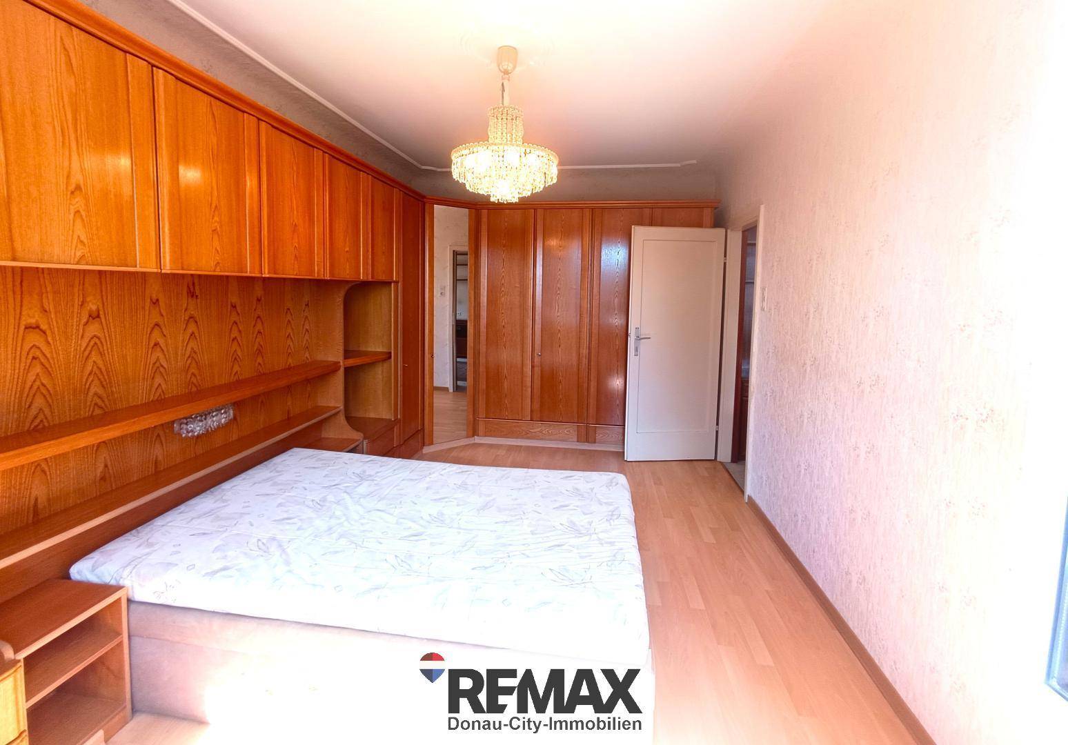 Schlafzimmer mit großem Bett, Holzeinbauschränken und einem Kronleuchter.