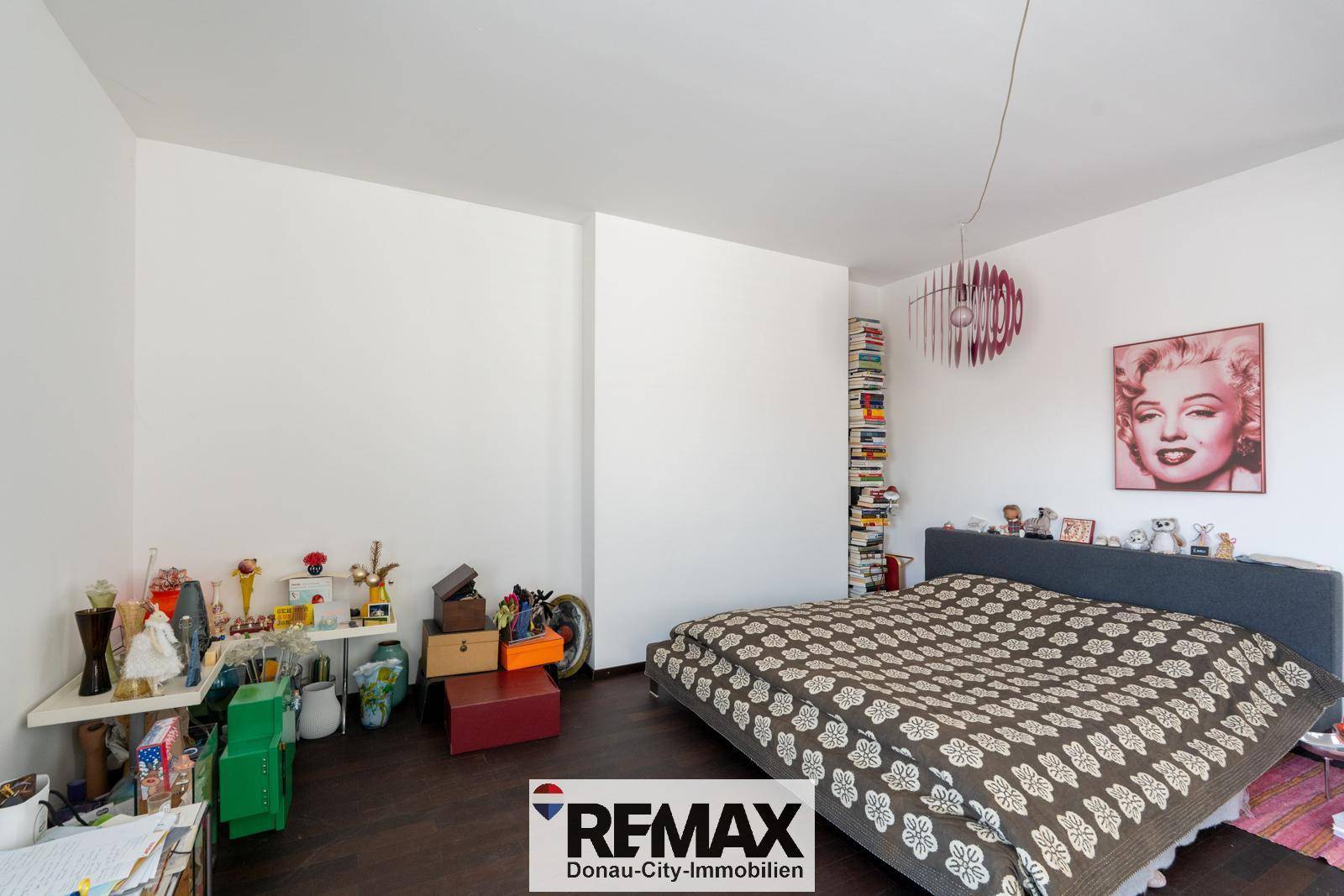 Schlafzimmer mit dunklem Holzboden und einem großen Bett, dekoriert mit einem Pop-Art-Bild.