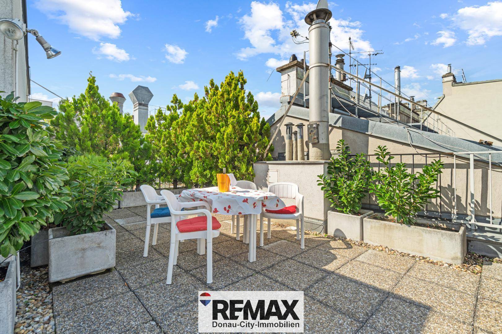 Möblierte Dachterrasse mit Esstisch und Stühlen, umgeben von Pflanzen und mit Blick auf die Stadt.