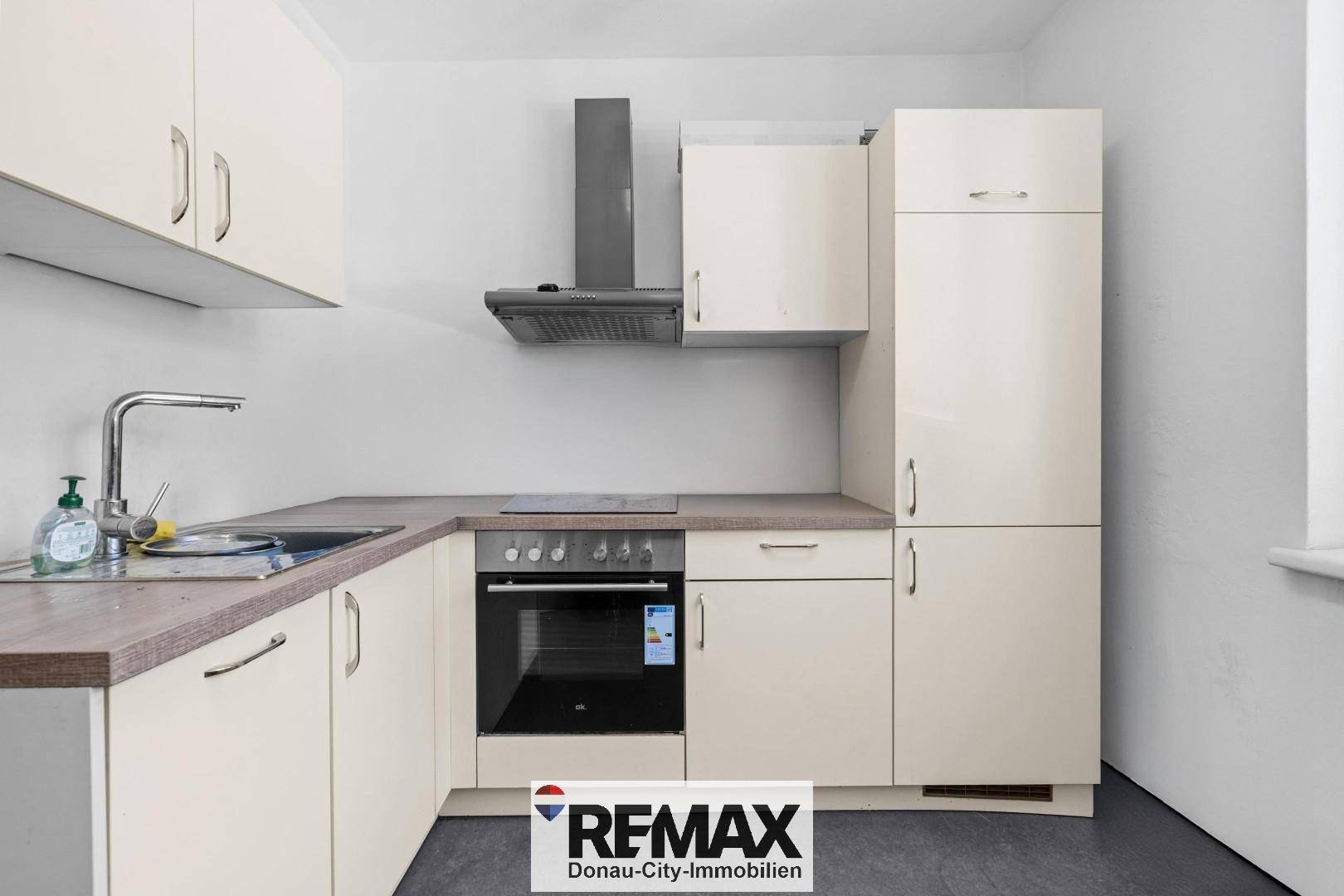 Funktionale Küche mit beigen Schränken, Holzarbeitsplatte, Spüle, Backofen und Induktionskochfeld.